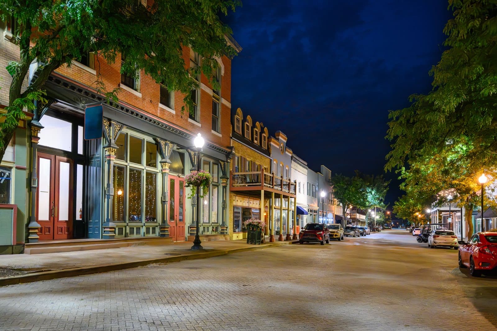 A small town main street in the evening, storefronts lit
